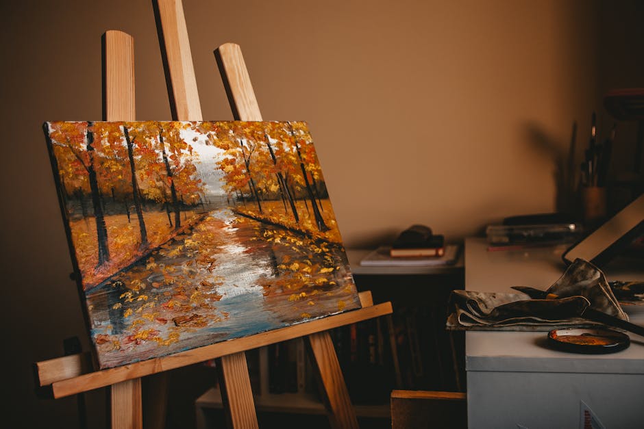 An oil painting of a fall landscape with vivid colors displayed in an artist's studio on a wooden easel.